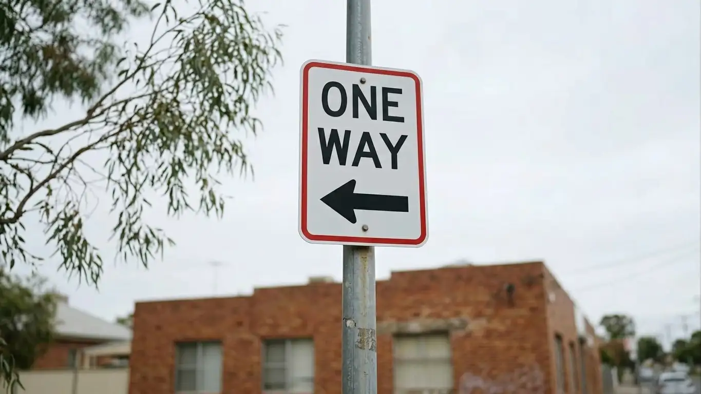 One-way street sign photographed against an overcast urban sky