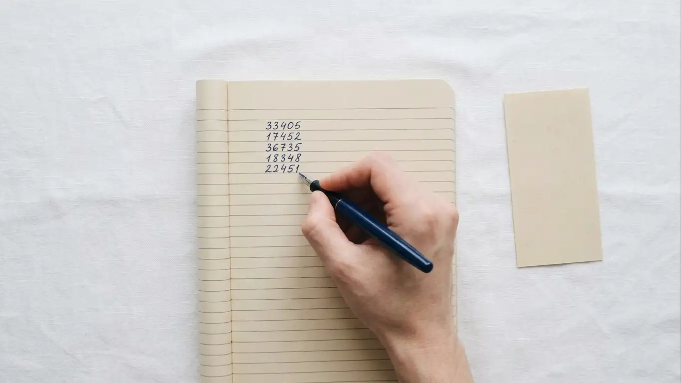 Hand writing session amounts in a notebook, single voucher slip set aside on the desk